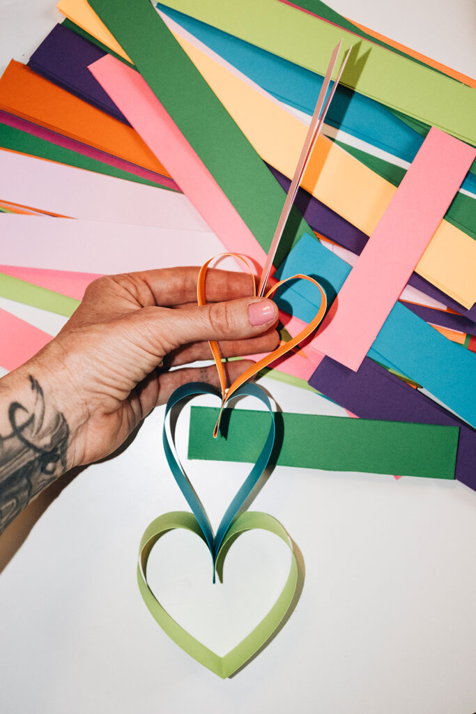 Lass uns eine Herz-Girlande aus Papierstreifen basteln.